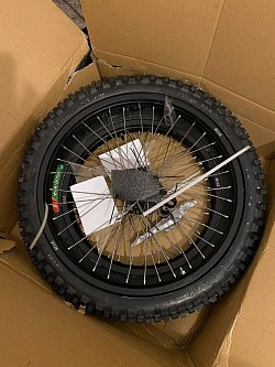 rear wheel for a Surron dirt bike. Helpful information includes:  It has a black rim with silver spokes and a knobby tire for off-road use.  The tire size and other markings are visible on the sidewall. It may come with accessories like rim locks, bands, and tools.  Rear-wheel drive systems in vehicles send power to the rear wheels.  Rear-wheel drive can offer better handling due to more balanced weight distribution.   $400