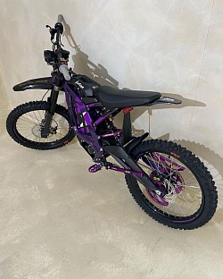 purple Surron Light Bee X electric dirt bike. Key features and information about the Surron Light Bee X include:  Type: Electric dirt bike, blending elements of a dirt bike and mountain bike. Brand: Surron. Model: Light Bee X. Motor: Electric, brushless. Battery: 48V, with a range of up to 80 miles on a single charge. Speed: Up to 47 mph (73 km/h), depending on load and gearing. Weight: 47 kg plus battery. Upgrades: This model features custom purple graphics and anodized JFG components. Year: This bike is a 2023 model. Condition: New, with 0 miles on the clock. Extras: Comes with 2 keys, charger, certificate of ownership, tool kit, and owner's manual.