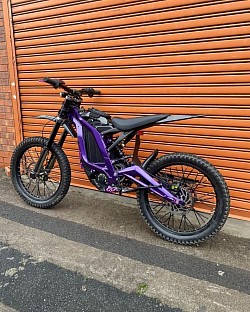 purple 2024 SUR-RON Light Bee X electric bike. Helpful information includes:  Part dirt bike, part mountain bike, all electric.  Easy to handle for beginners, but also suitable for experienced riders.  Top speed of 47 mph (73 km/h).  Range of up to 80 miles on a single charge, depending on conditions.  Net weight of 47 kg plus the battery.  Wheel size: Front/Rear 19 x 1.4 Alloy Hubs.  Tire size: Front/Rear 70/100-19 CST.  Some models come with a 75V battery, with a max speed of 70-75 km/h.
